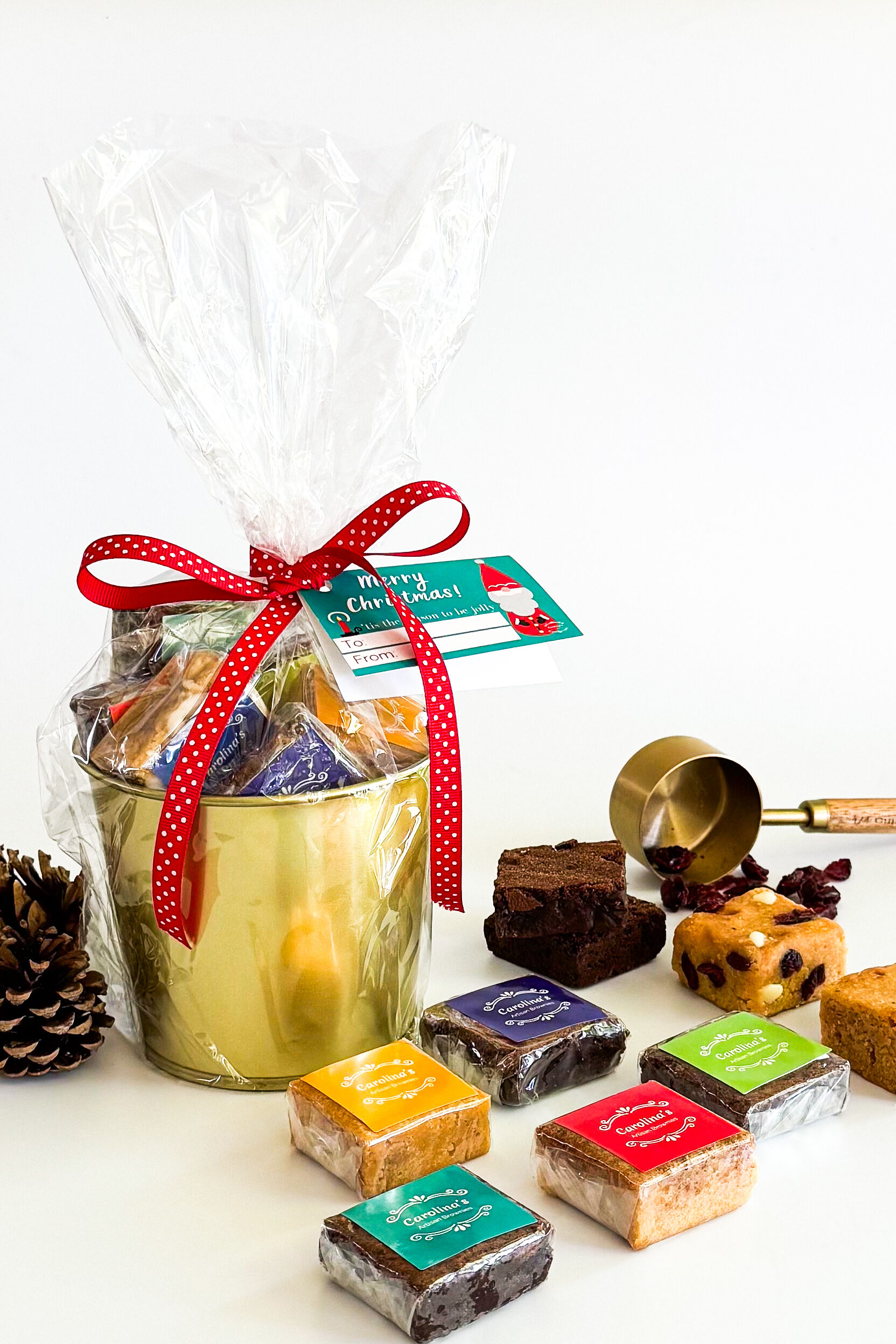 A golden bucket filled with brownies and wrapped with cellophane and red ribbon with five brownies wrapped with colourful labels in front plus more brownies in the back 